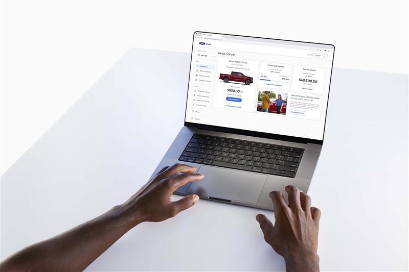 Hands reaching for a laptop computer with a screen showing the Ford Credit website.